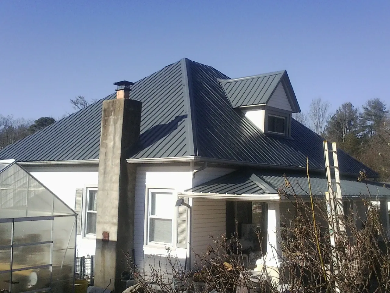 Dark blue standing seam metal roof on a white farmhouse with dormer — Slate & Tile Roof Repair by Roofing Brothers in Lloyd