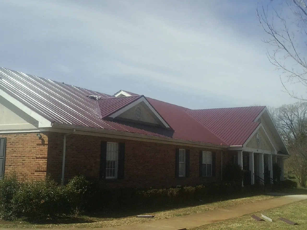 Red metal roof with gabled entries on a long brick building, from a Hail Damage Roof Repair job in Lloyd