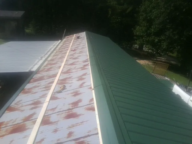 Old rusted panels beside newly installed green metal roofing — Wind Damage Roof Repair by Roofing Brothers in Lloyd