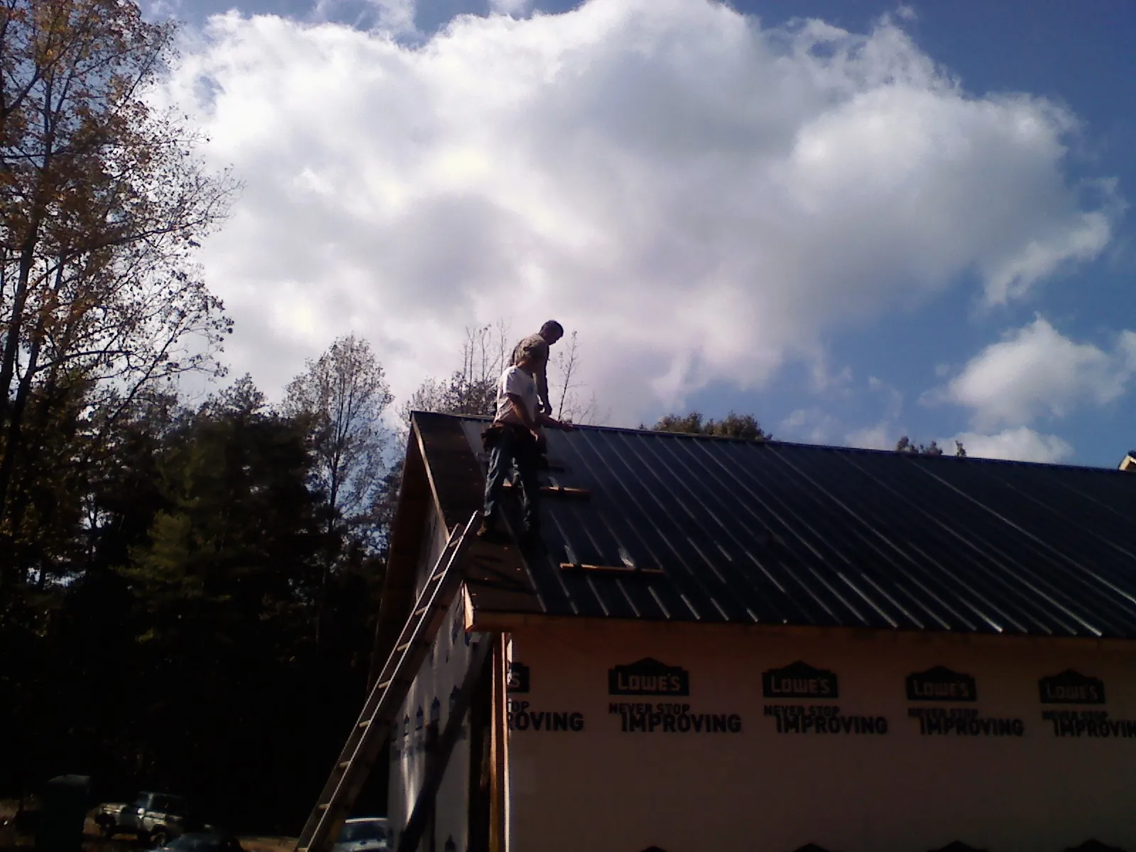 Roofer fastening dark metal panels high against a cloudy sky, from a Roof Inspection job in Lloyd